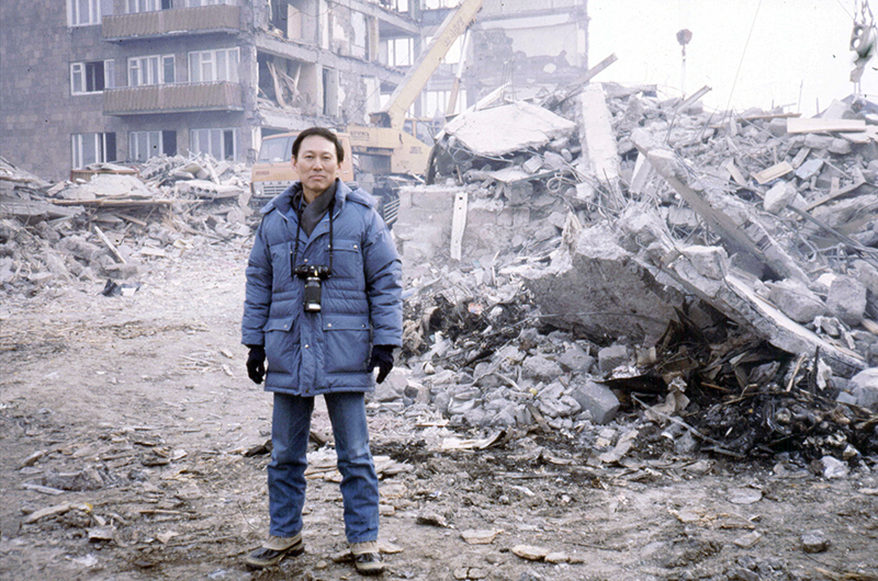 Lew standing in front of rubble from a building