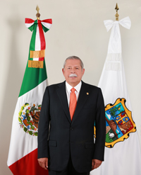 Texas CAEE alumnus Egidio Torre-Cantú standing in front of two flags